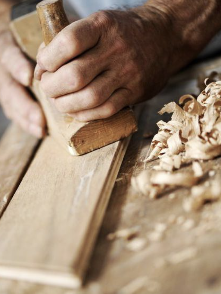 Kreatives & Rustikales Hände, die mit einem Hobel Holz bearbeiten, um eine glatte Oberfläche zu erzielen.